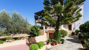 A two-story building with a stone-paved entrance, surrounded by potted plants and trees. - Small Apartmentcomplex in Village of Prinès near Rethymnon (Rethymno)