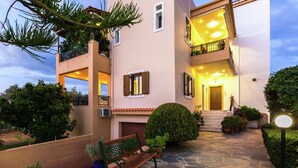 A two-story building with a stone-paved courtyard, a bench, and potted plants. - Small Apartmentcomplex in Village of Prinès near Rethymnon (Rethymno)