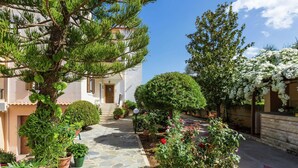A stone-paved courtyard with potted plants, a well-maintained garden, and a building with a wooden door and steps. - Small Apartmentcomplex in Village of Prinès near Rethymnon (Rethymno)