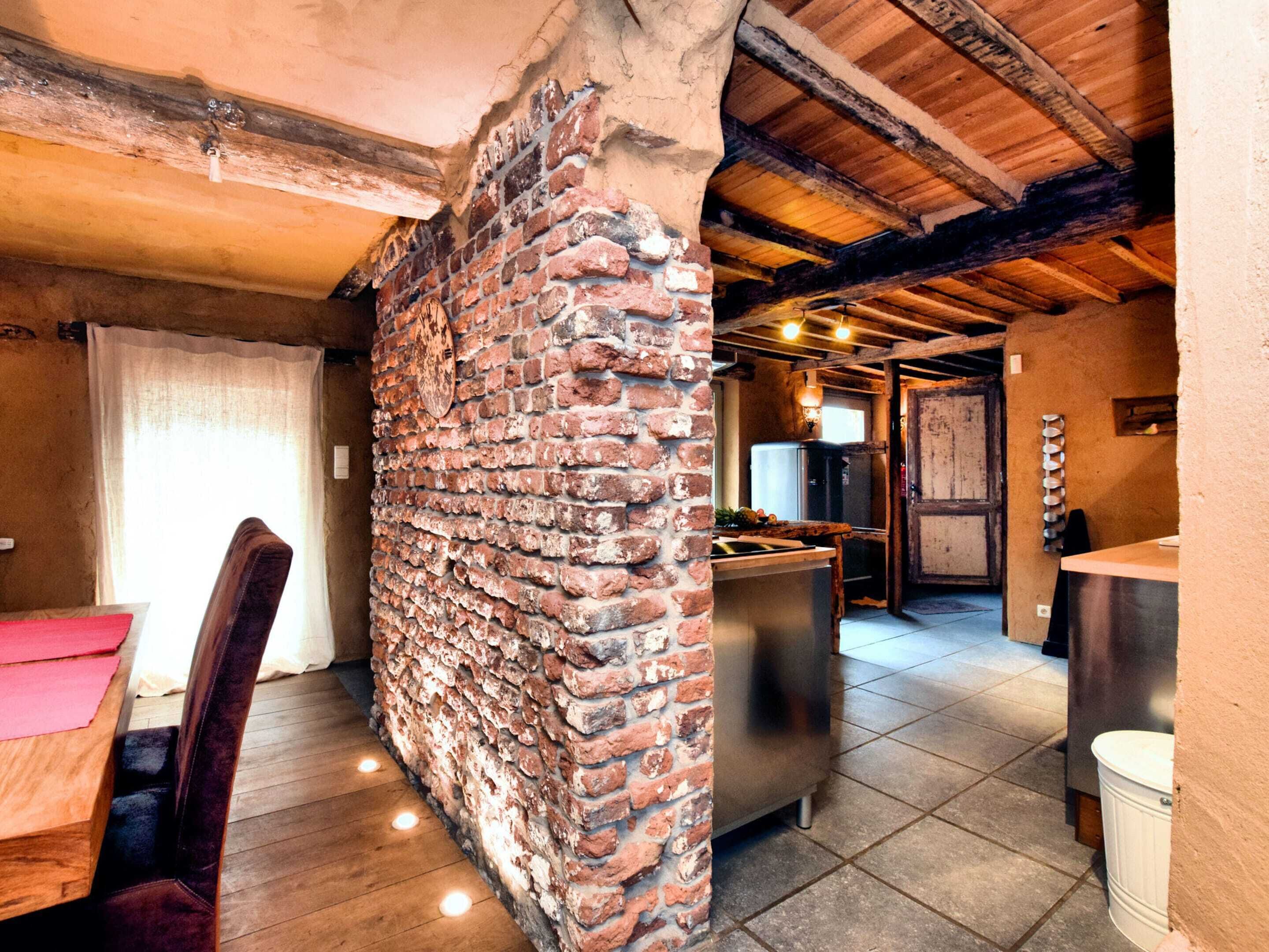 A rustic kitchen with exposed brick walls, wooden beams, and a modern stainless steel refrigerator.