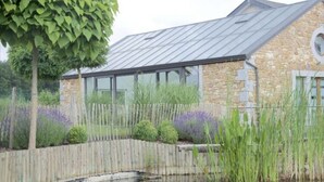 A stone building with a metal roof, surrounded by a wooden fence and a pond. - Luxury Spa Retreat in Theux (Theux)