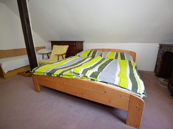 Habitación con una cama individual de estructura de madera, una colcha a rayas, una pequeña silla, un aparador de madera y una mesita de noche.