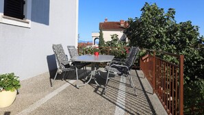 Une terrasse avec une table et des chaises, un pot de fleurs et une rambarde en métal.