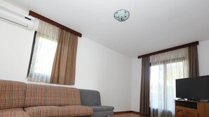 Un salon avec un canapé, un téléviseur posé sur un meuble en bois et une horloge au mur.