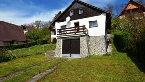 A two-story house with a stone foundation, a wooden balcony, and a black door.