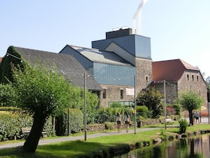 Stunning building with a modern design, featuring a prominent chimney and skylights, surrounded by a beautifully maintained garden with a pond.
