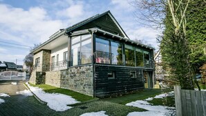 Une maison à deux étages avec des murs en pierre, un balcon doté de rampes en métal et une terrasse en bois.