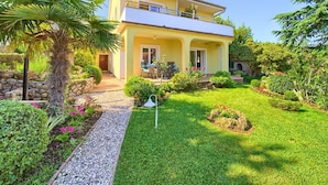 A two-story house with a balcony, surrounded by a well-maintained garden with various plants and a pathway. - Pleasant Apartment in Vantacici Amid the Sea (Malinska-Dubasnica)