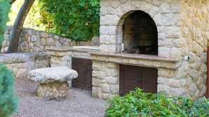 A stone-built outdoor kitchen with a tiled roof, a stone bench, and a stone wall in a garden setting. - Pleasant Apartment in Vantacici Amid the Sea (Malinska-Dubasnica)