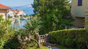 A well-maintained garden with a lamp post, a stone wall, and a view of a body of water with boats. - Pleasant Apartment in Vantacici Amid the Sea (Malinska-Dubasnica)