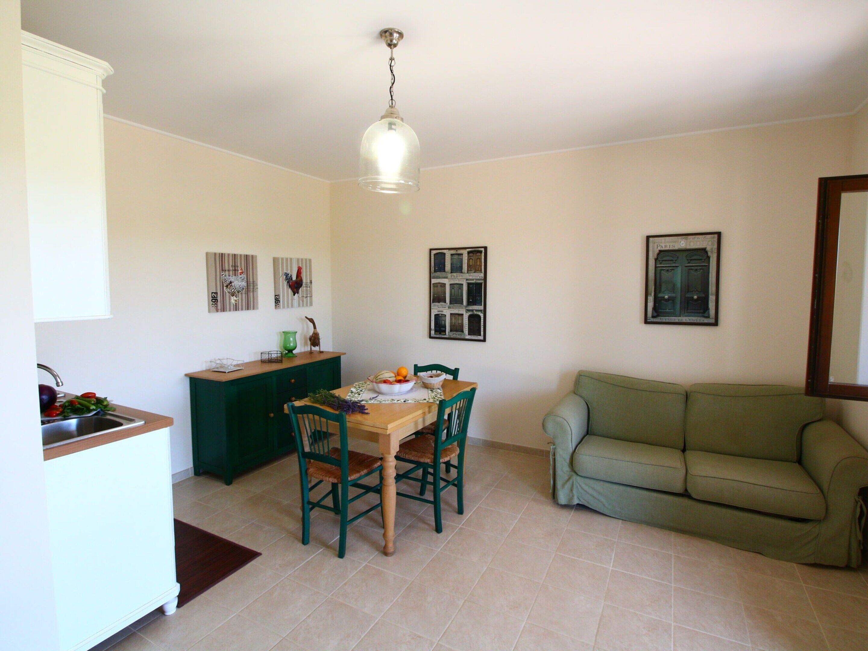 A dining area with a wooden table, two chairs, a green sofa, and a kitchen area with a sink and cabinets.