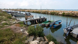 A marina with several boats docked, surrounded by rocky shores and sparse vegetation. - Loving Apartment in Rosolina Mare near Venice (Rosolina)