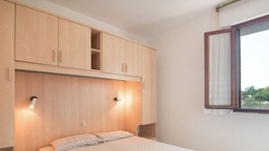 A bedroom with a bed, wooden cabinets, and a window with curtains. - Loving Apartment in Rosolina Mare near Venice (Rosolina)