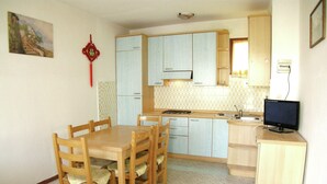 A compact kitchen with a dining table, chairs, a small refrigerator, and a computer on a counter. - Simplistic Apartment in Rosolina Mare near Sea (Rosolina)