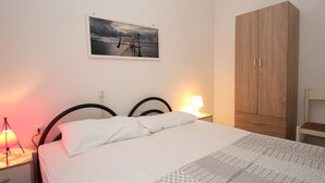 A bedroom with a bed, a nightstand with a lamp, a wooden wardrobe, and a framed picture on the wall. - Simplistic Apartment in Rosolina Mare near Sea (Rosolina)