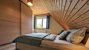 A cozy bedroom with a wooden ceiling, a bed with patterned pillows, a window with curtains, and a radiator. - Spacious Flat in Wilhelmshof near Lake (Usedom)