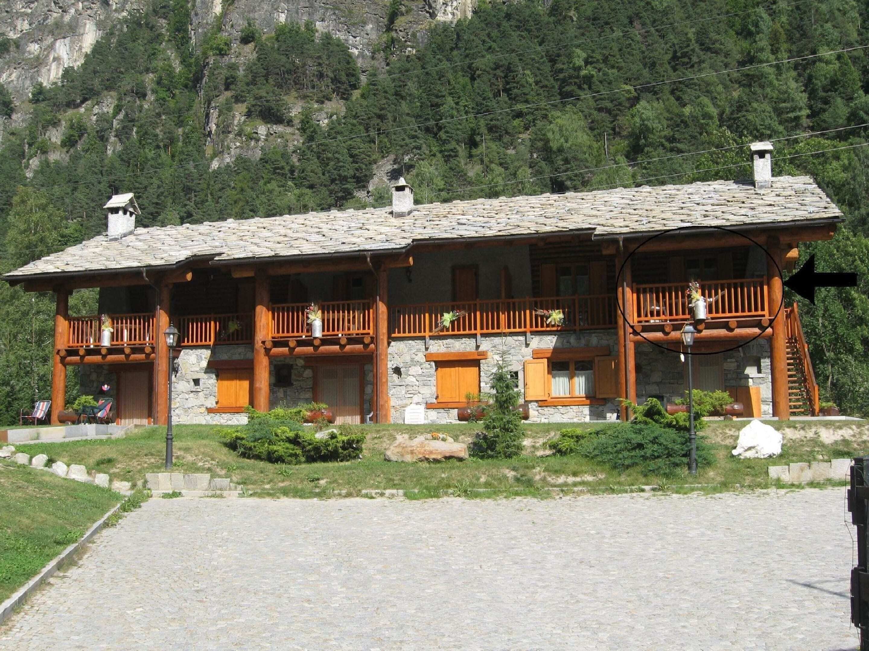 Un edificio de estilo chalé con paredes de piedra y balcones de madera, con montañas al fondo.