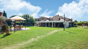 Relax in a serene outdoor setting surrounded by lush greenery and trees, with comfortable seating areas under umbrellas.