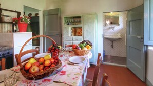 A kitchen with a dining table set for two, featuring a basket of fruit, a plate, and a glass.