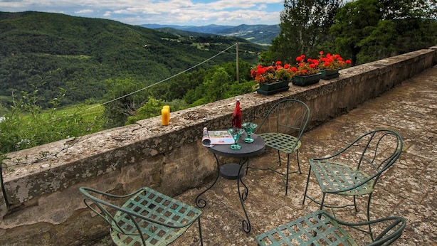 A terrace with a table and chairs overlooking a lush valley.
