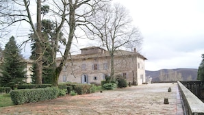 A historic stone building with a courtyard, surrounded by mature trees and a stone wall.