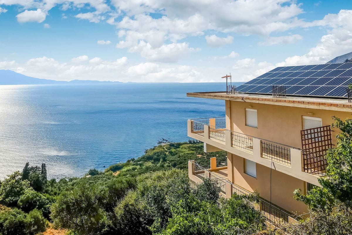 A coastal building with a balcony and solar panels, overlooking the sea.