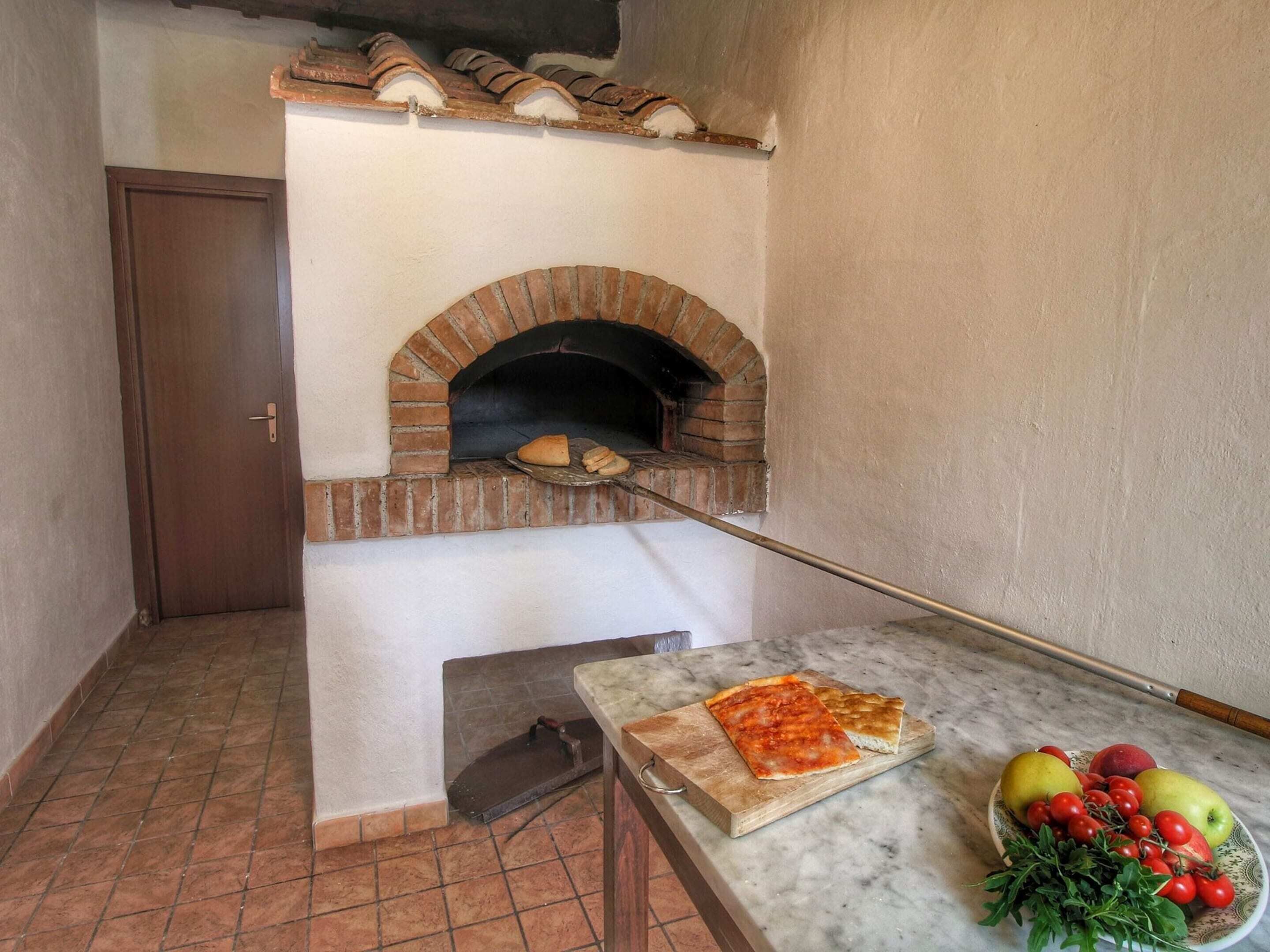 A kitchen with a brick oven, a cutting board with pizza, and a bowl of fruit.