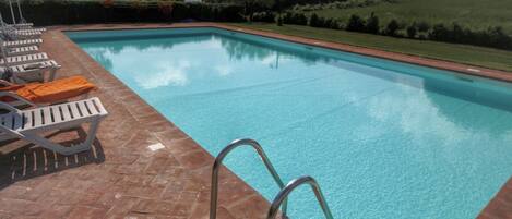 Une piscine à l’eau d’un bleu cristallin, entourée d’une terrasse carrelée et de chaises longues.