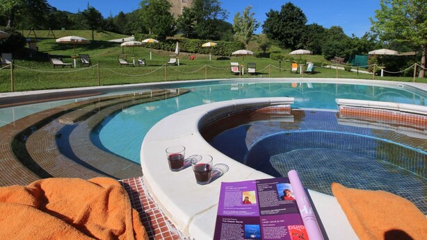 A pool area with a hot tub, lounge chairs, and a view of a hill with a building. - Country House Getaway in Apecchio (Apecchio)