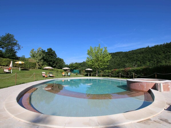 A circular pool with a clear blue water surface, surrounded by a stone deck and a low brick wall. - Country House Getaway in Apecchio (Apecchio)