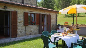 A stone building with a patio area featuring a table set for a meal, outdoor chairs, and a yellow umbrella. - Country House Getaway in Apecchio (Apecchio)