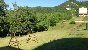 A grassy area with a swing set, a small building, and a railway track. - Country House Getaway in Apecchio (Apecchio)