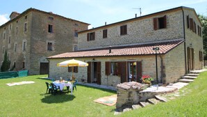 A stone building with a tiled roof, a patio with a table and chairs, and a small garden area. - Country House Getaway in Apecchio (Apecchio)