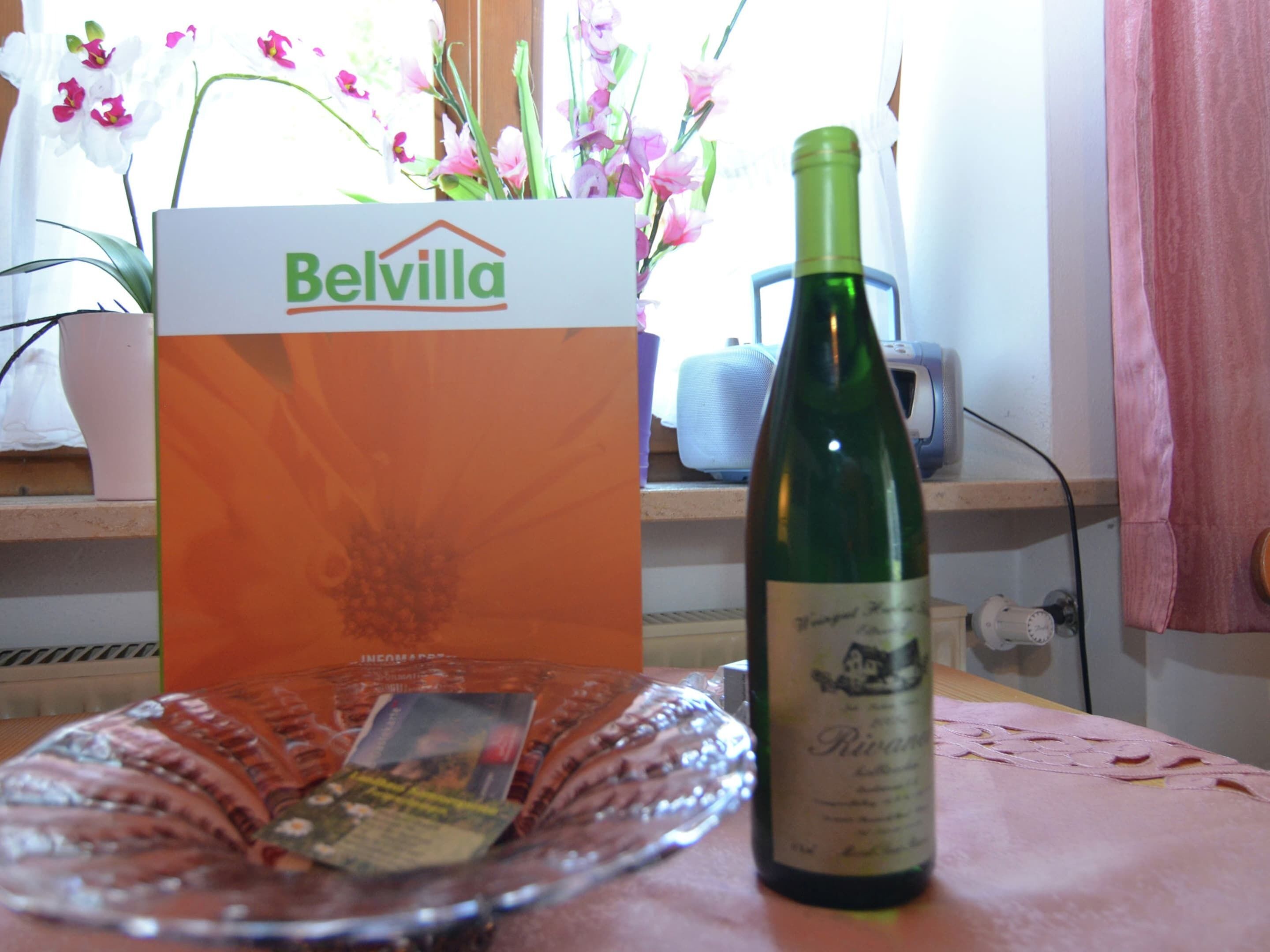Una bottiglia di vino, un bicchiere e un cartello Belvilla su un tavolo.