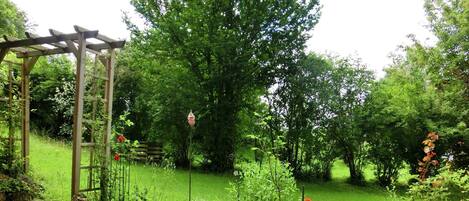 Ein Garten mit einer Holzpergola, einem Rasen und verschiedenen Pflanzen.