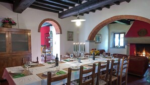 A dining area with a long table set for a meal, wooden chairs, a brick fireplace, and a red archway. - Holiday Home in Dicomano (Dicomano)