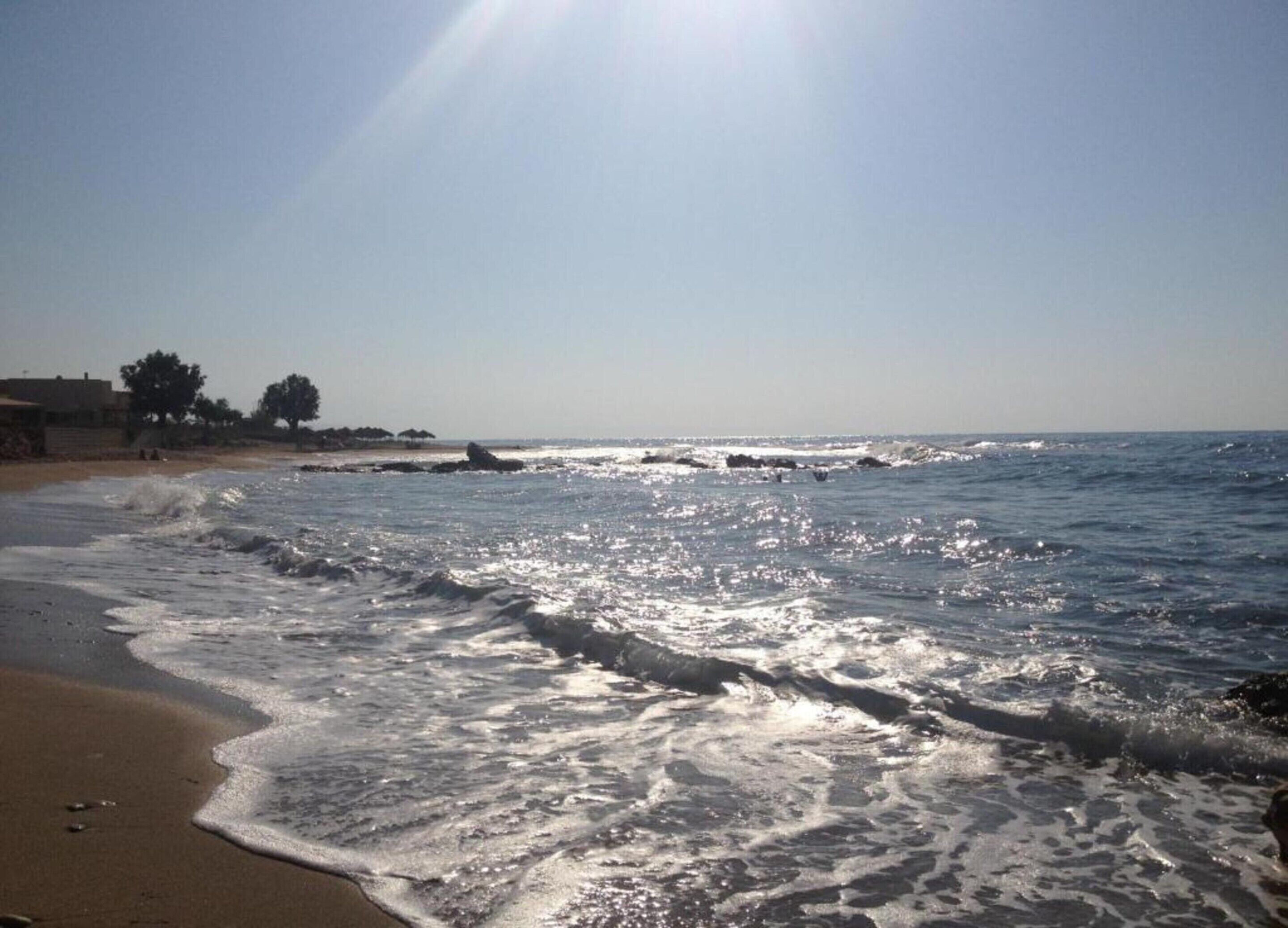 A beach with waves, a clear sky, and distant buildings.