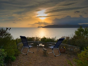 Two lounge chairs facing a sunset over a body of water with a distant landmass.