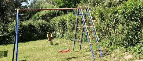 A swing set with a ladder in a grassy area with trees in the background.