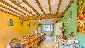 A dining area with a long table, chairs, and a kitchen area with a refrigerator and sink.