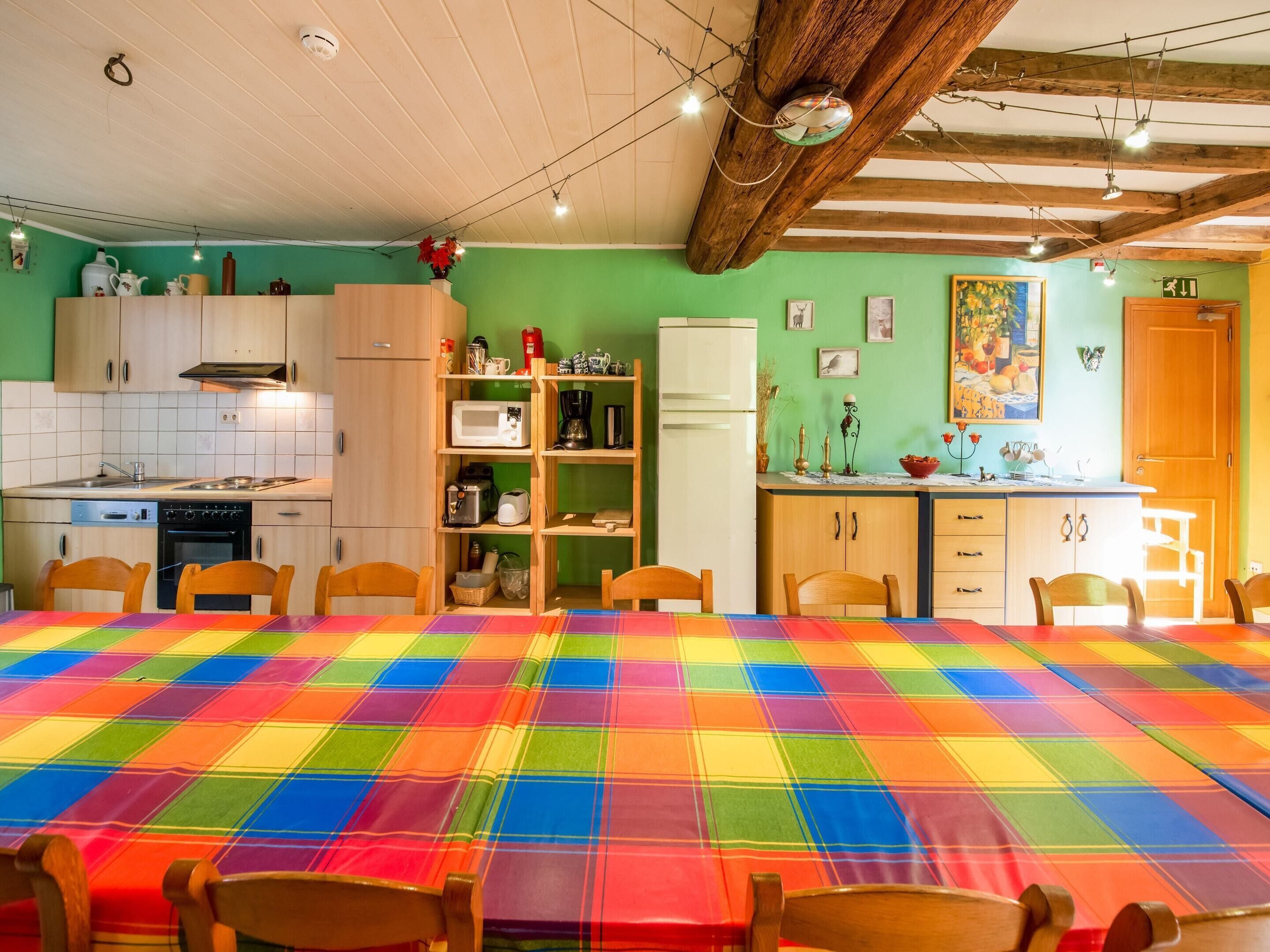 A kitchen with wooden cabinets, a microwave, and a refrigerator. There is a dining table with a colorful tablecloth and wooden chairs.