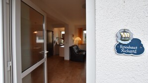 Interior de hotel com porta de entrada de vidro, área de estar com sofá de couro e placa na parede com a inscrição 'Ferienhaus Richard'.