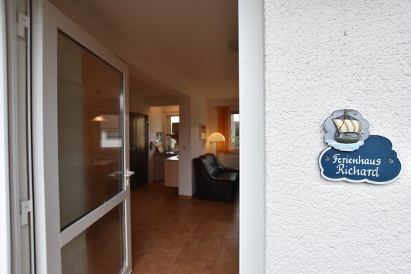 Interior de un hotel con entrada por puerta de vidrio, zona de estar con sofá de cuero y un letrero en la pared que dice 'Ferienhaus Richard'.