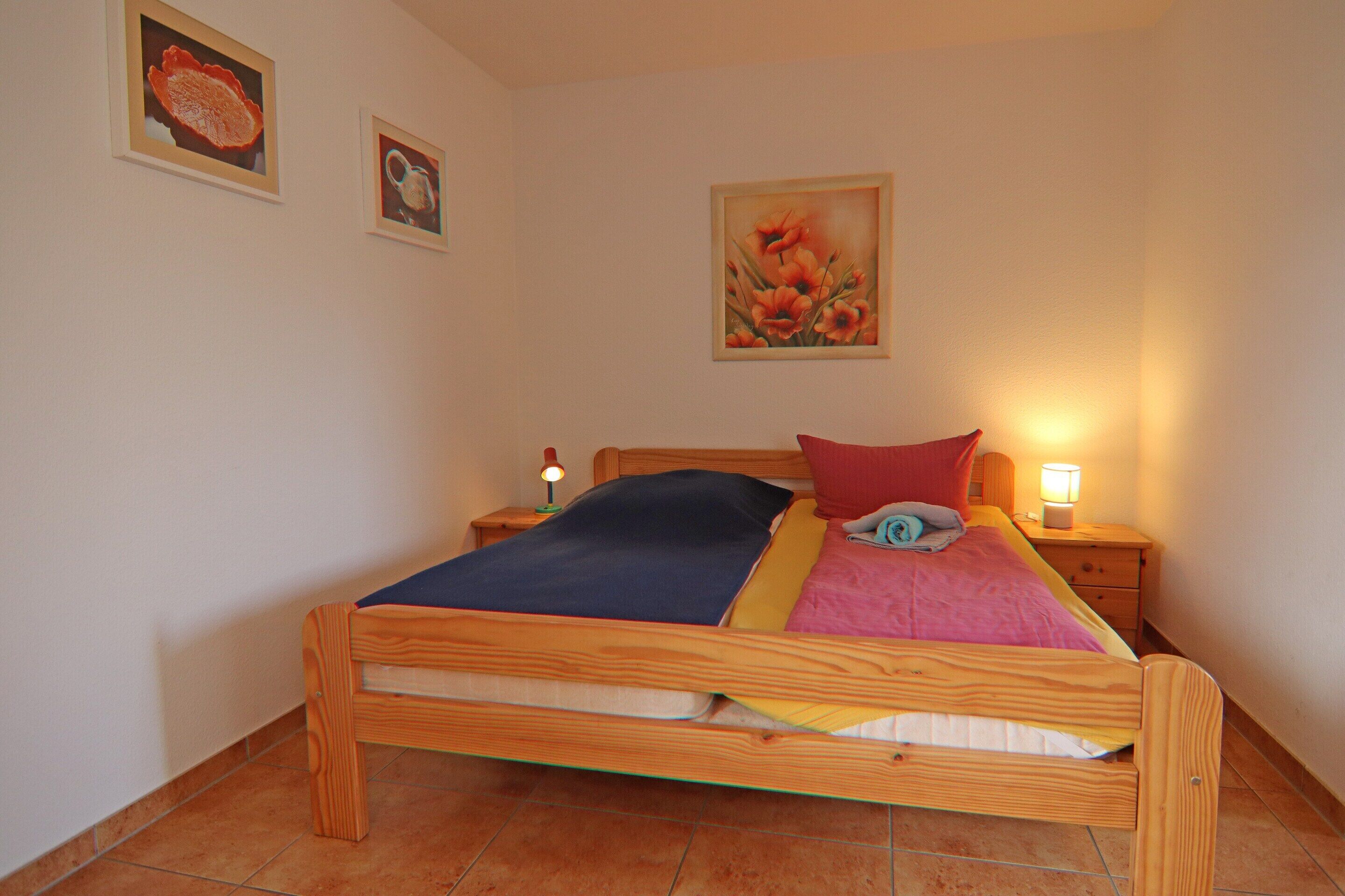 A single bed with a wooden frame, a bedside table with a lamp, and two framed pictures on the wall.