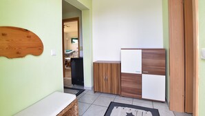 A compact kitchen with a wooden cabinet and a white fridge, a small bench, and a tiled floor. - Modern Bungalow in Damshagen in Terrace, Garden and Barbecue (Damshagen)