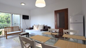 Quarto moderno com cama, sofá, mesa de jantar com cadeiras, TV na parede e geladeira.