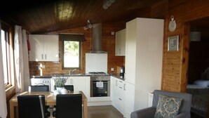 Une cuisine chaleureuse, aménagée dans le style d’un chalet, avec des murs en bois, une table à manger entourée de chaises et un fauteuil gris agrémenté d’un coussin à motifs.