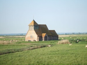 A single-story brick building with a conical roof and a small tower, surrounded by a grassy field with sheep grazing. - Cosy Pine Lodge With far Reaching Country Views and Large sun Deck (Romney Marsh)