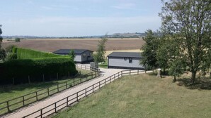 Un paysage rural avec un chemin de gravier menant à un petit bâtiment, entouré de champs et d’un arbre.