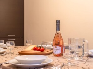 Ein Tisch ist gedeckt mit Tellern, einer Flasche Pinot Grigio Rosé, einem Holzbrett mit Tomaten und einer Kanne.